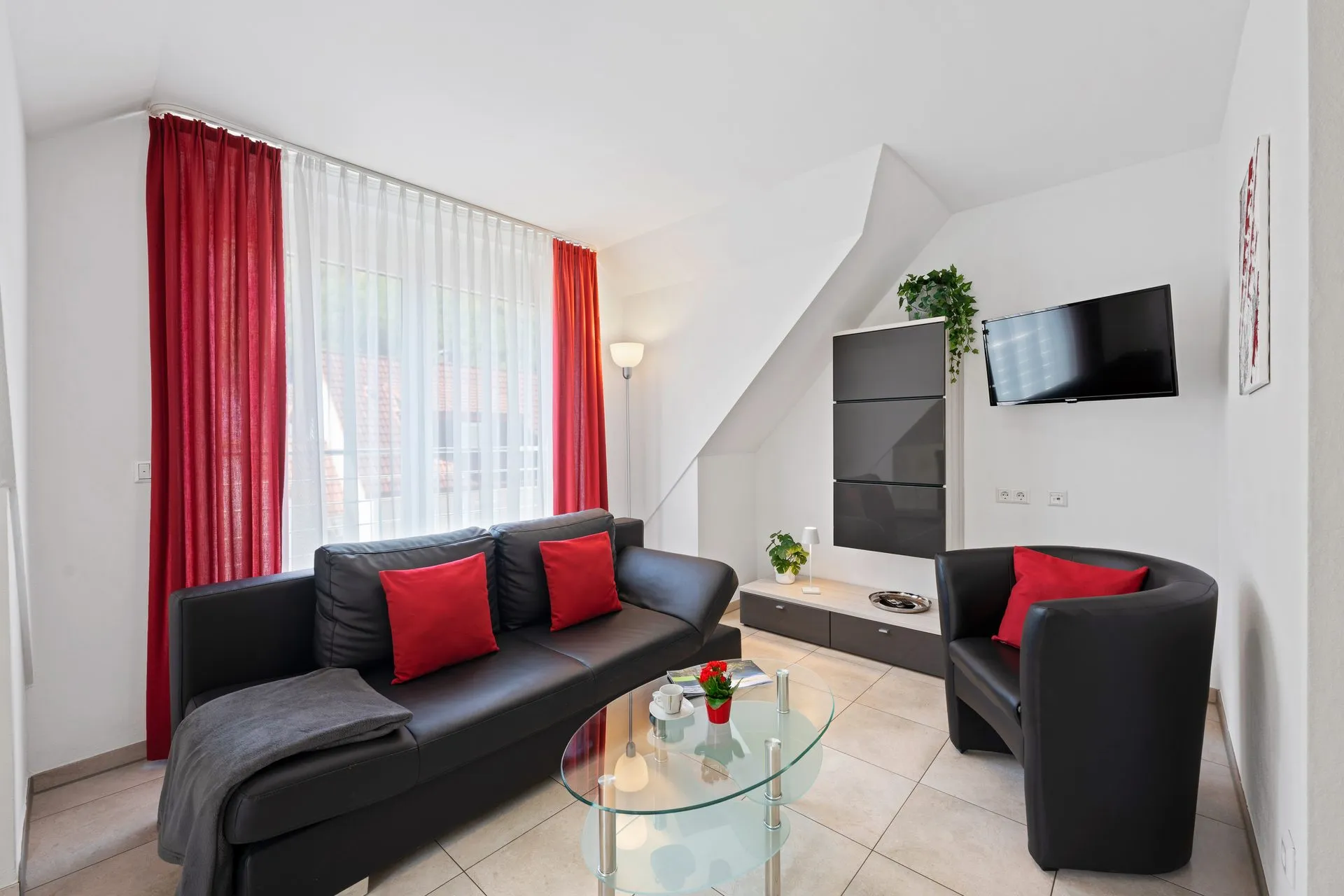 Wohnbereich mit roten Vorhängen, dunklem Sofa und Sesseln