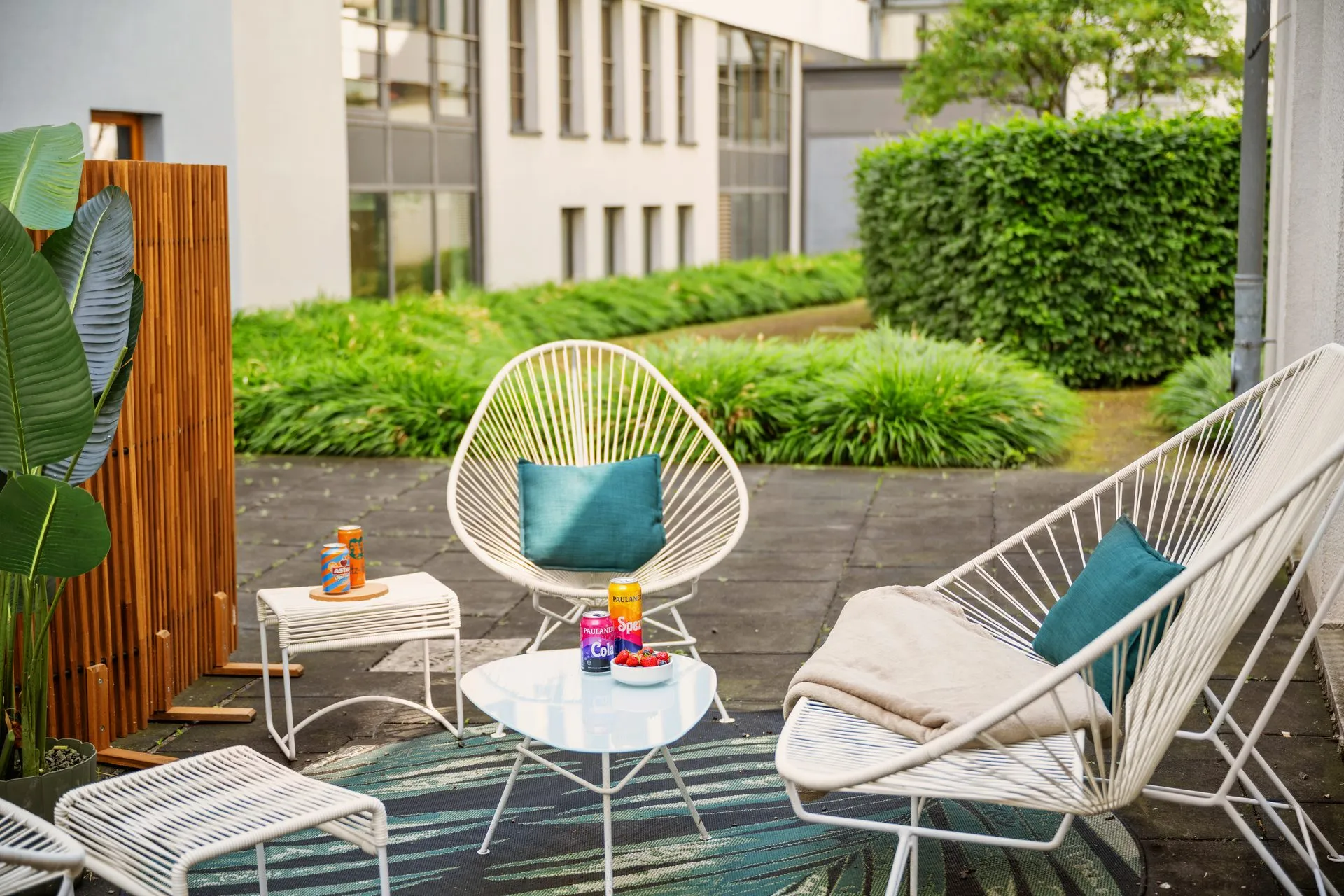 Terrasse mit weißen Drahtsesseln und Beistelltisch vor einer Hecke