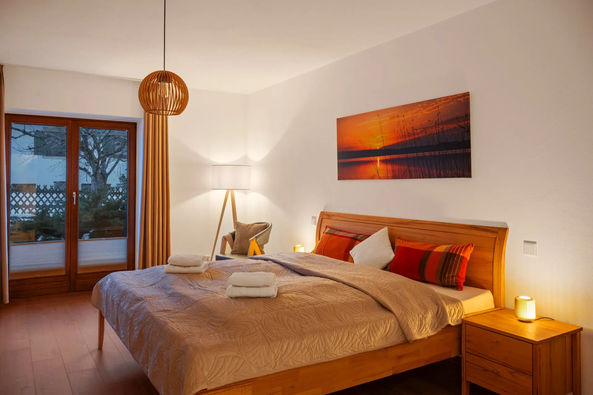 Schlafzimmer mit Doppelbett in warmem Lampenlicht, frische Handtücher auf der Tagesdecke