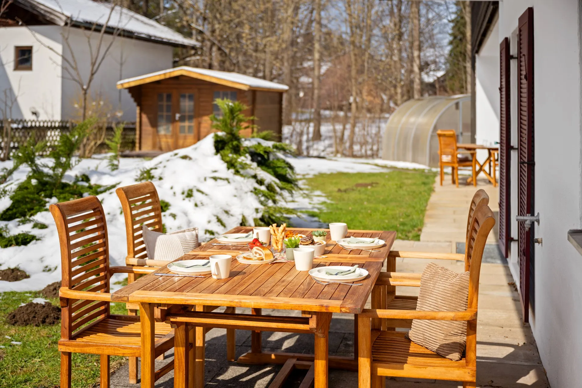 Gedeckter Holztisch auf der Terrasse, im Garten dahinter liegt noch Schnee