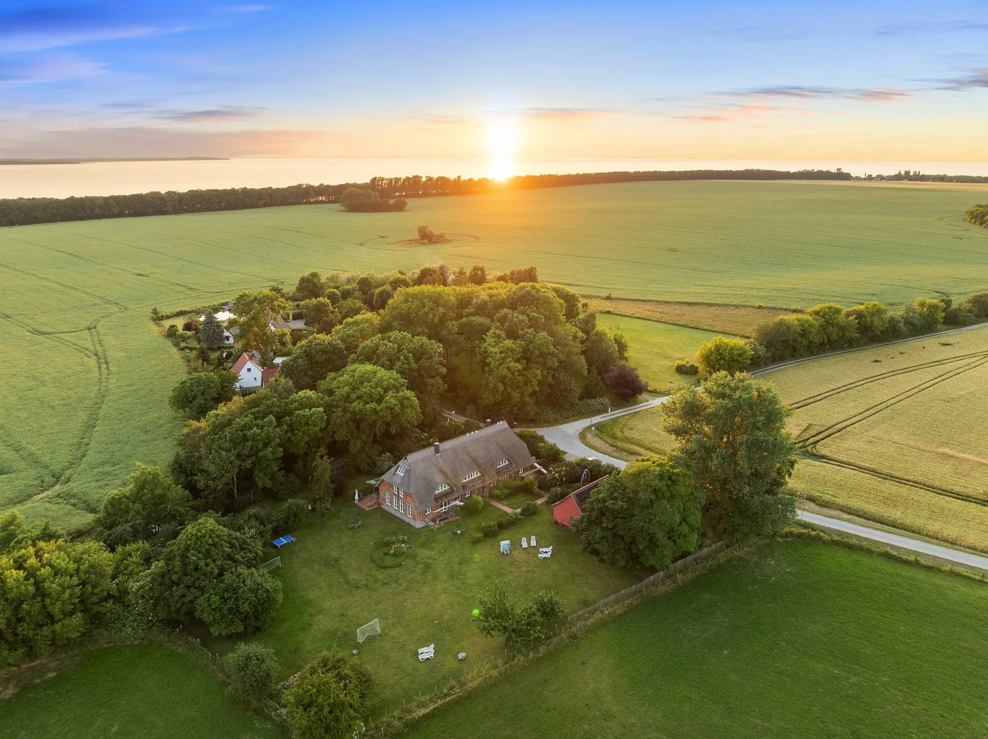 Luftaufnahme des Anwesens zwischen Feldern und Baumgruppen im Sonnenuntergang