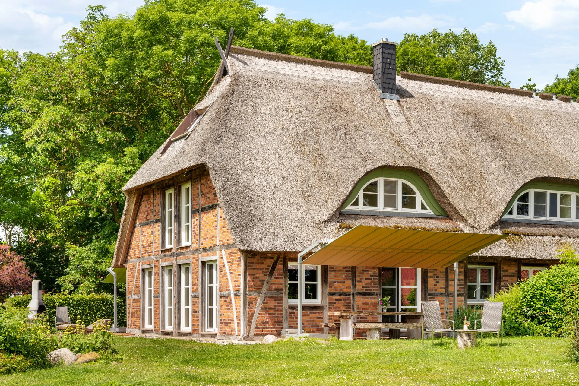 Reetgedecktes Backsteinhaus mit geschwungenen Gauben und Terrasse im Grünen