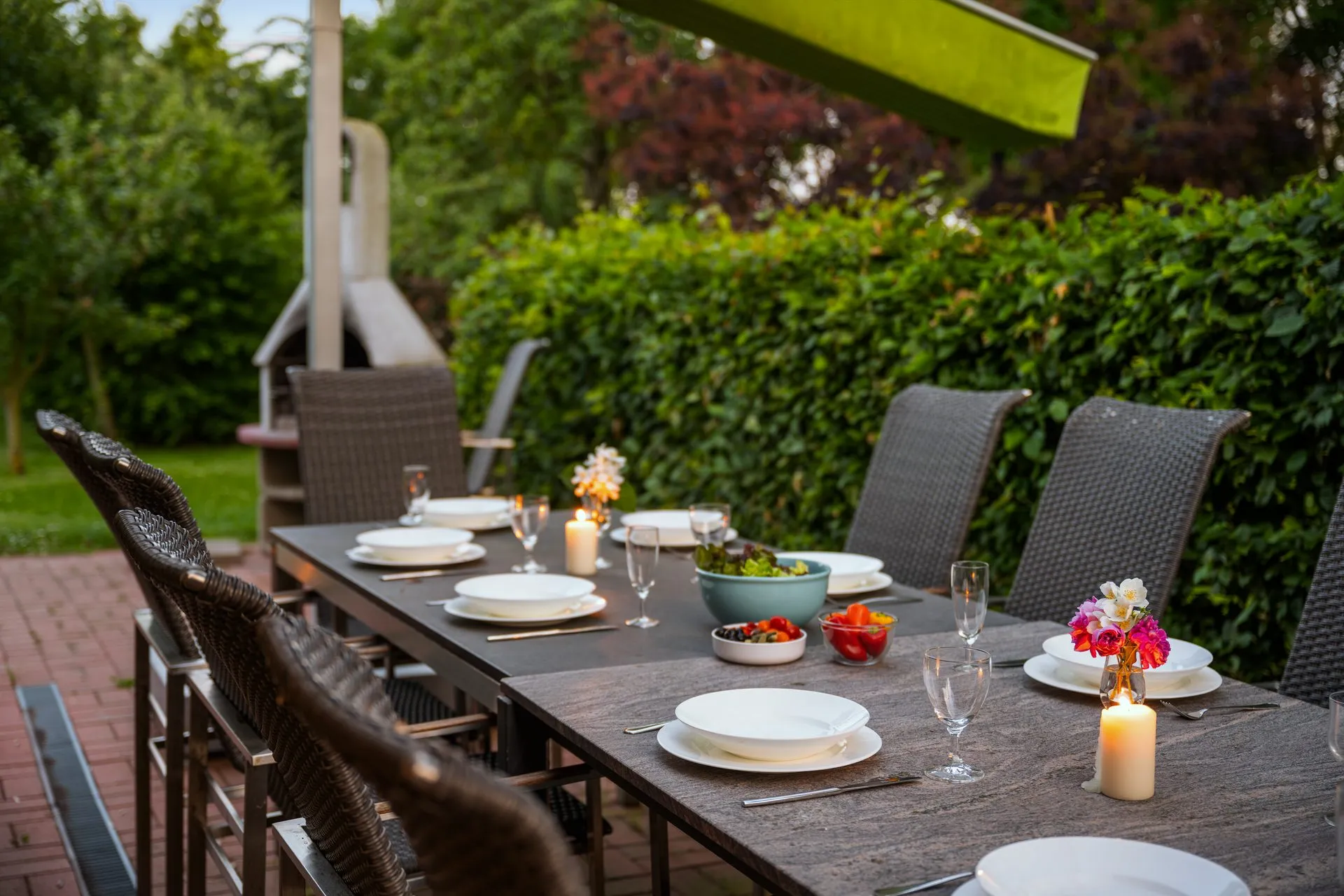 Gedeckter Gartentisch mit Kerzen und Blumen vor einer hohen Hecke