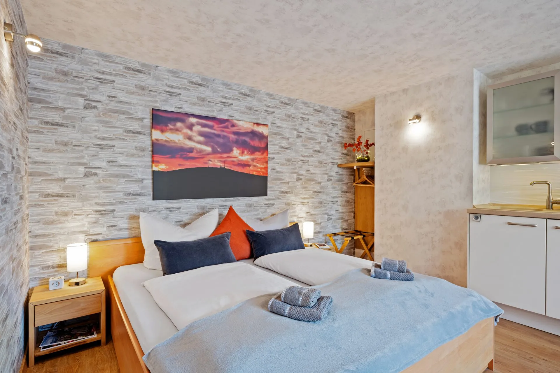Schlafzimmer mit heller Steinwand und Doppelbett in warmem Licht